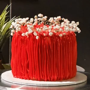 This beautiful cake is made with soft, fluffy vanilla cake layers and smooth, creamy buttercream. The cake is finished with textured red buttercream icing that gives it a bold and elegant look. Delicate white floral decorations on top add a lovely touch of charm.