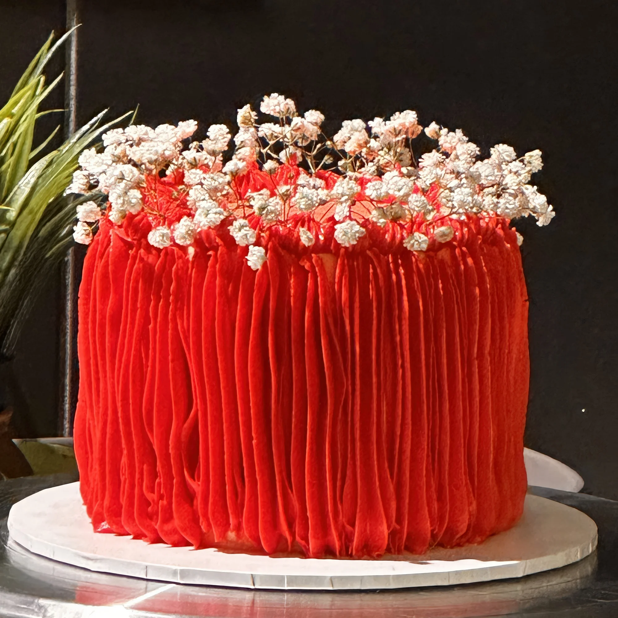 This beautiful cake is made with soft, fluffy vanilla cake layers and smooth, creamy buttercream. The cake is finished with textured red buttercream icing that gives it a bold and elegant look. Delicate white floral decorations on top add a lovely touch of charm.